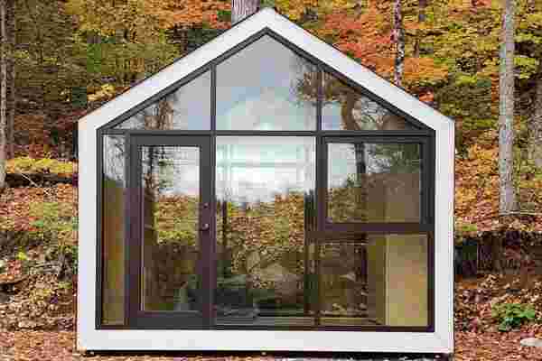 This tiny cabin shaped like the home icon features floor-to-ceiling facades for nature lovers!